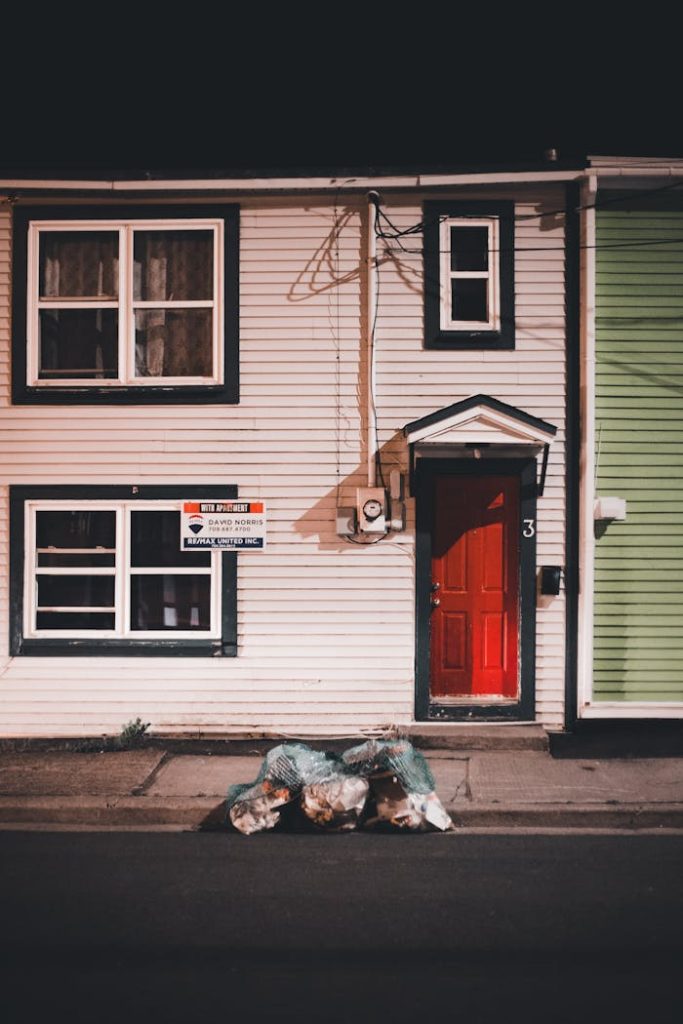 Cozy house facade with a striking red door, windows, and street lights at night.